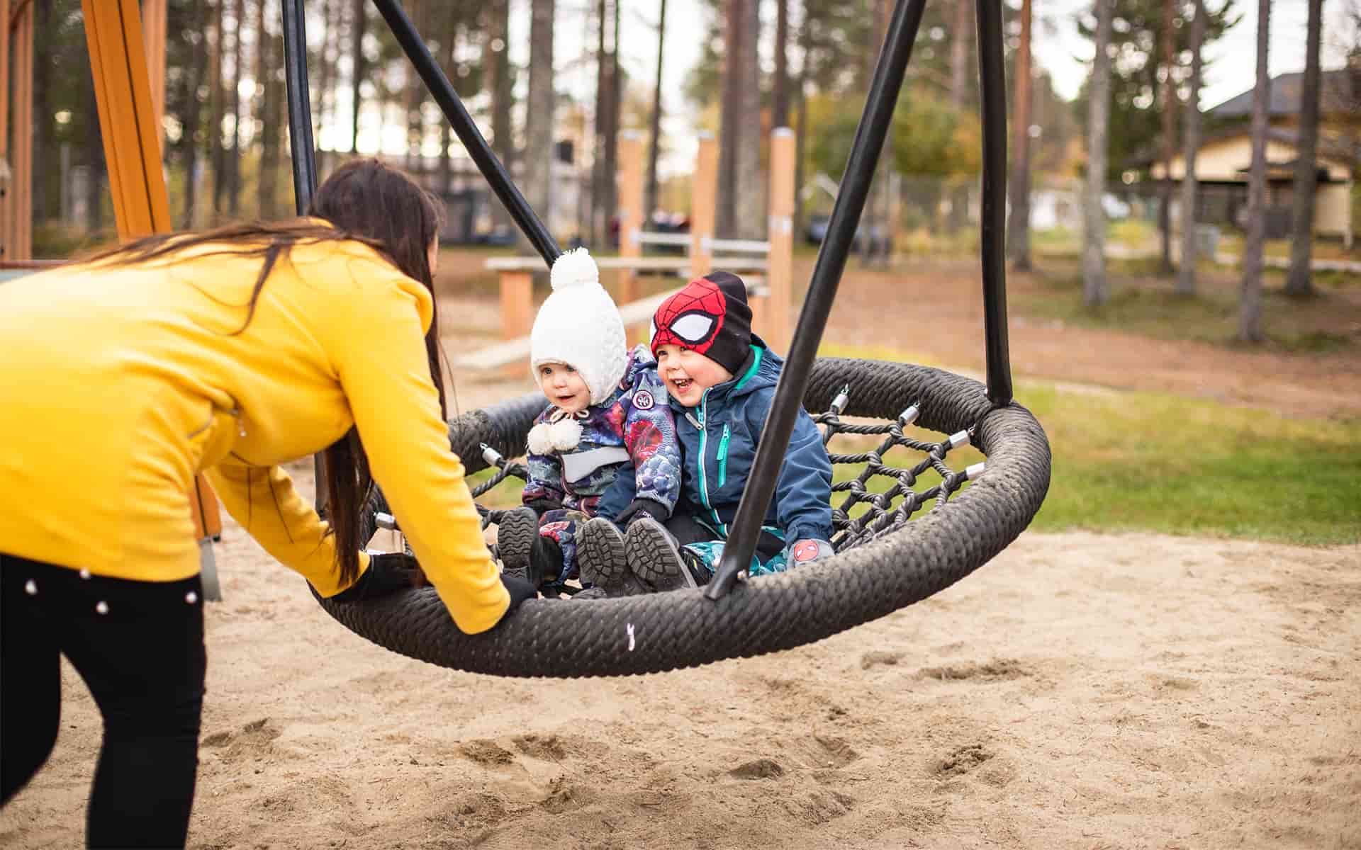 Aikuinen keinuttaa kahta lasta keinussa